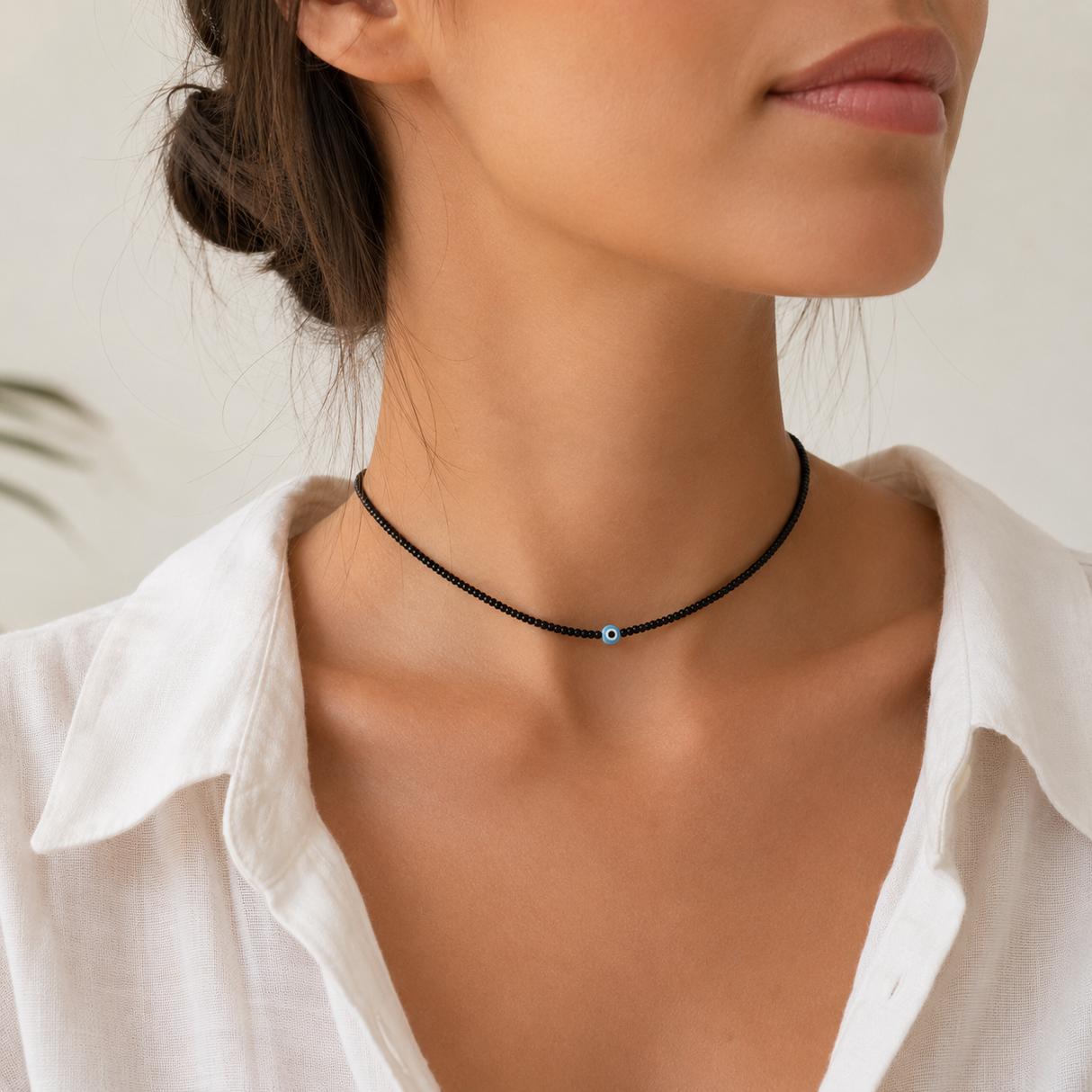 Woman wearing black tiny beaded evil eye choker necklace with a single pale blue evil eye bead, styled with a white collared shirt