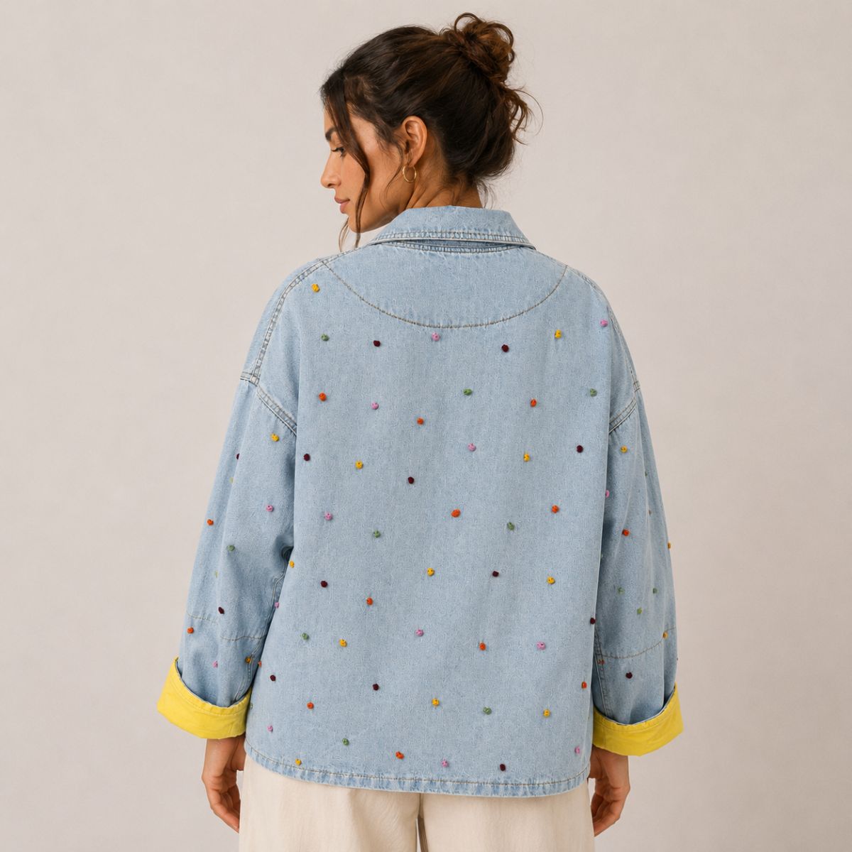 Back view of the Boutique Flo Confetti Embroidered Light Denim Jacket worn by a model, showing the multicolor embroidered dots across the back and yellow contrast cuffs