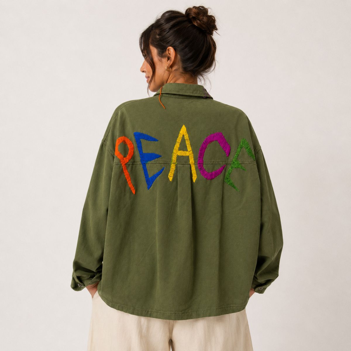 Back view of the Boutique Flo Peace Embroidered Green Jacket worn by a model, showing the hand-embroidered multicolor PEACE lettering across the olive cotton twill