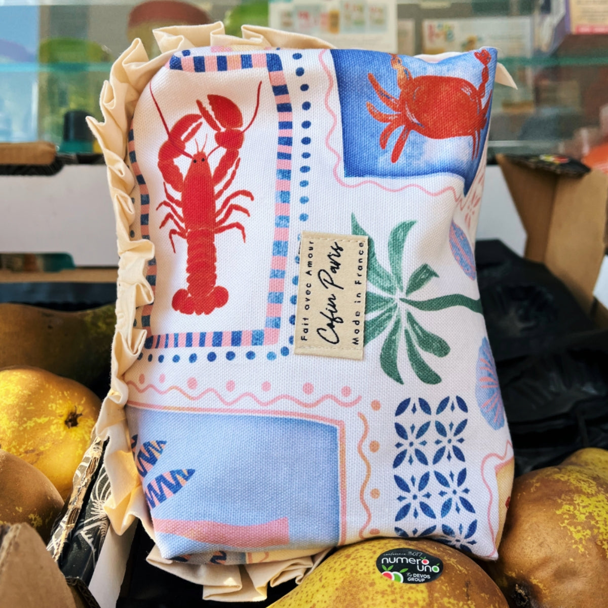 Medium Paola Riviera toiletry pouch displayed vertically alongside fresh produce, highlighting the woven Cofin Paris logo label.