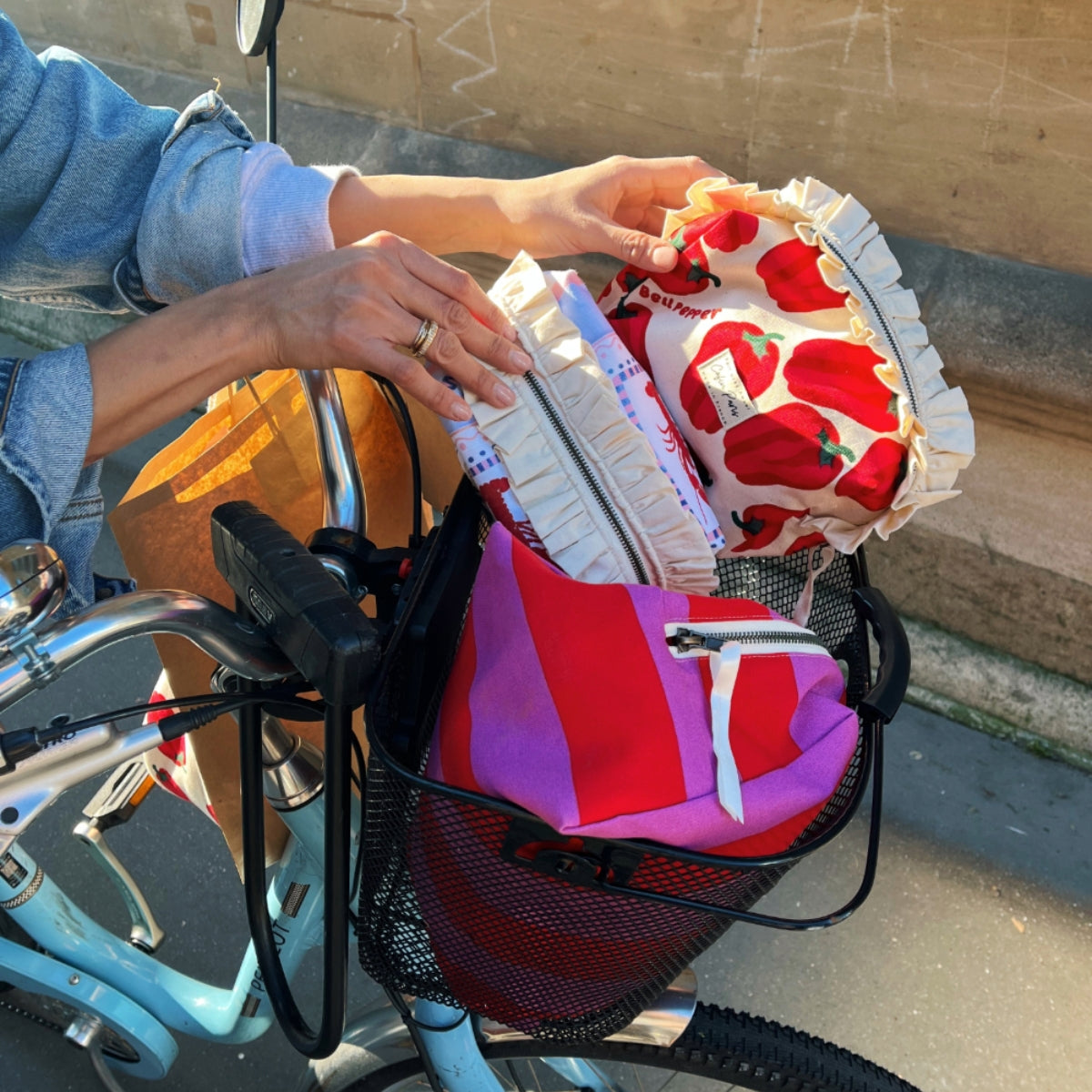 Lifestyle shot of Cofin Paris ruffled toiletry bags tucked inside a bicycle basket outdoors.