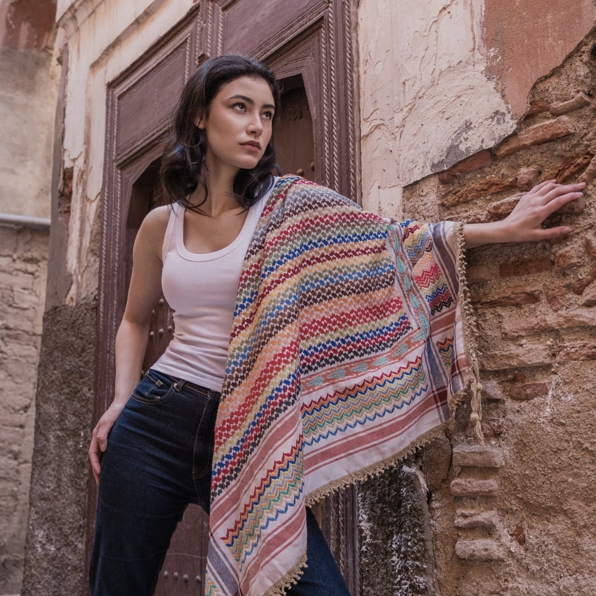 Model posing against an old brick doorway with SEP beige multicolor keffiyeh scarf draped open across her shoulder