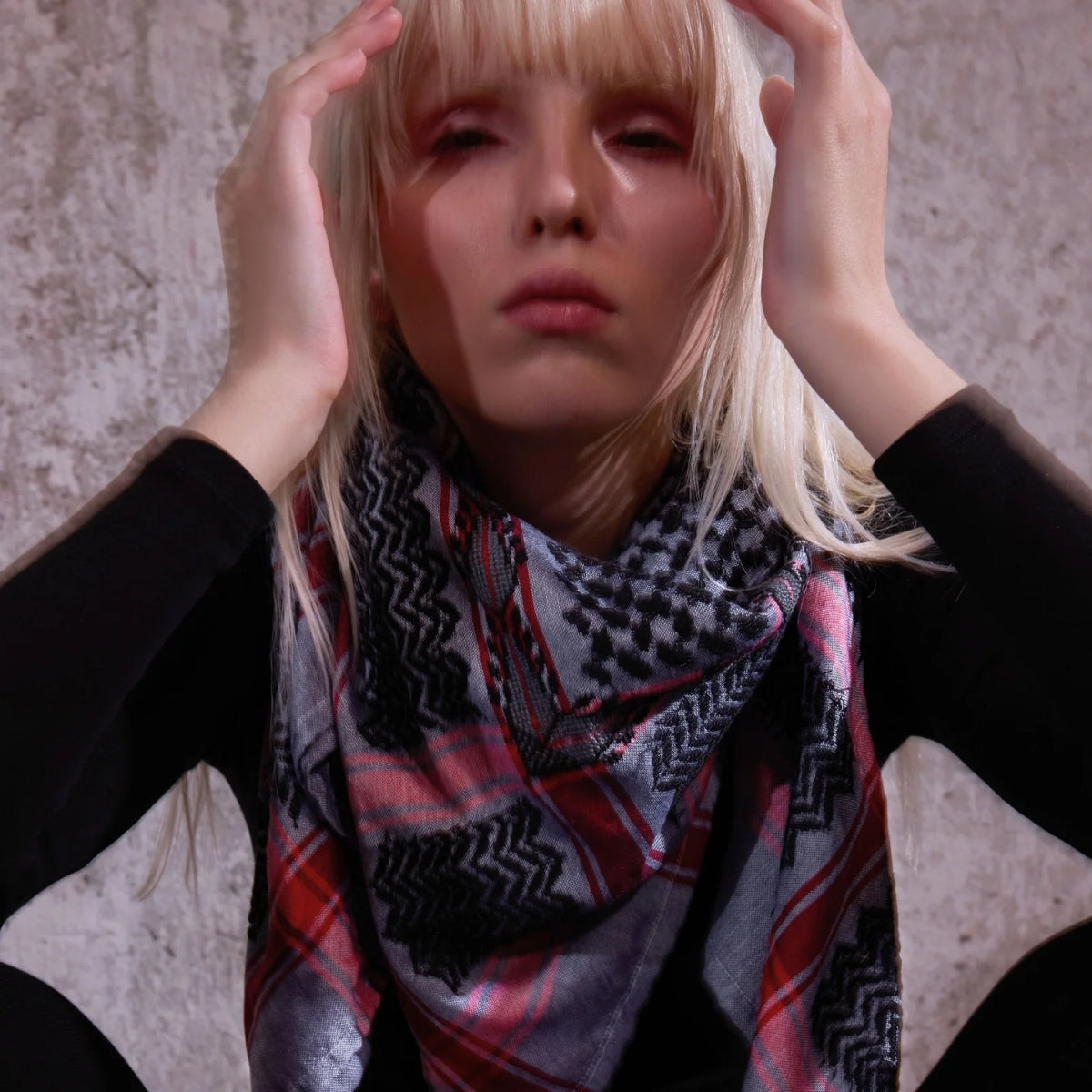 Close-up portrait of blonde model wearing SEP grey and black keffiyeh scarf styled around her neck over black clothing