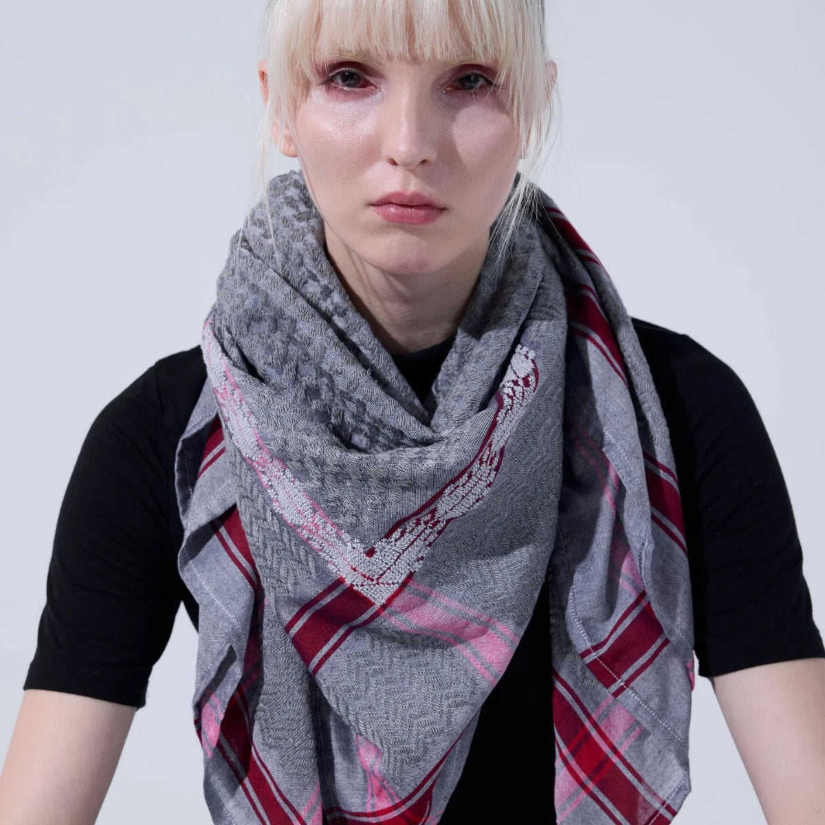 Front view portrait of model wearing SEP grey thalia keffiyeh scarf layered around her neck over a black top