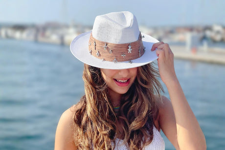 White embellished fedora statement hat with decorative band, styled for summer travel and resort wear
