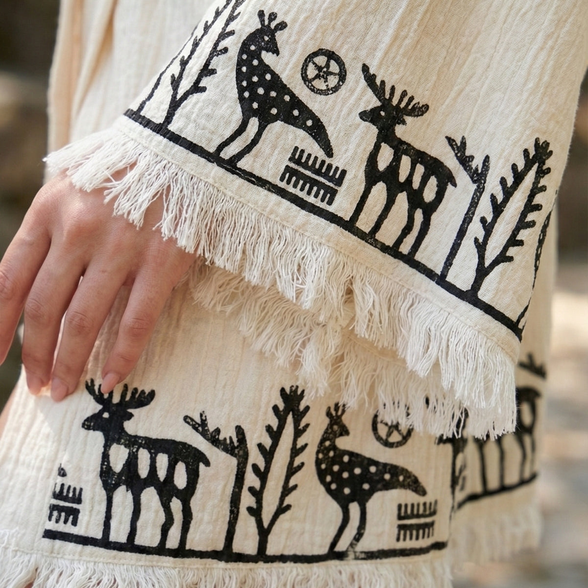 Close-up photo sleeves photo of the beige short kimono with black deer and tree patterns and white fringe print.
