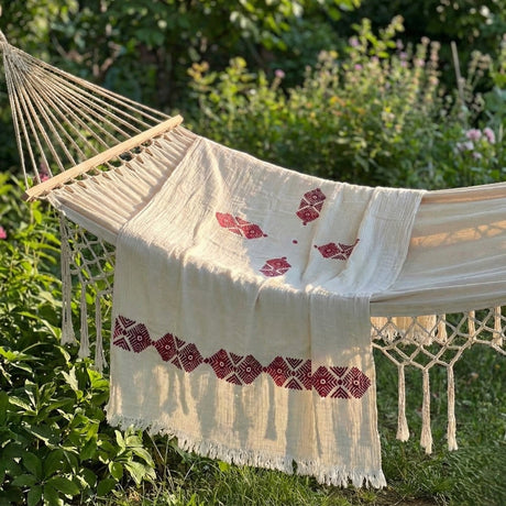 Hammock with a white shawl featuring red tribal patterns, set against a natural outdoor background.