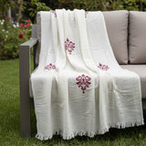 White printed shawl draped over a chair outdoors with greenery in the background