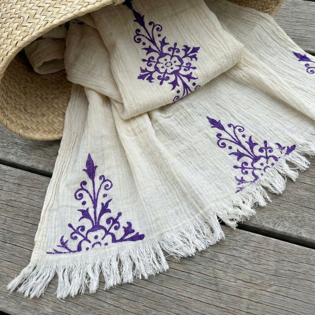 White scarf with purple floral patterns and fringes on a wooden surface