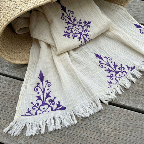 White scarf with purple floral patterns and fringes on a wooden surface