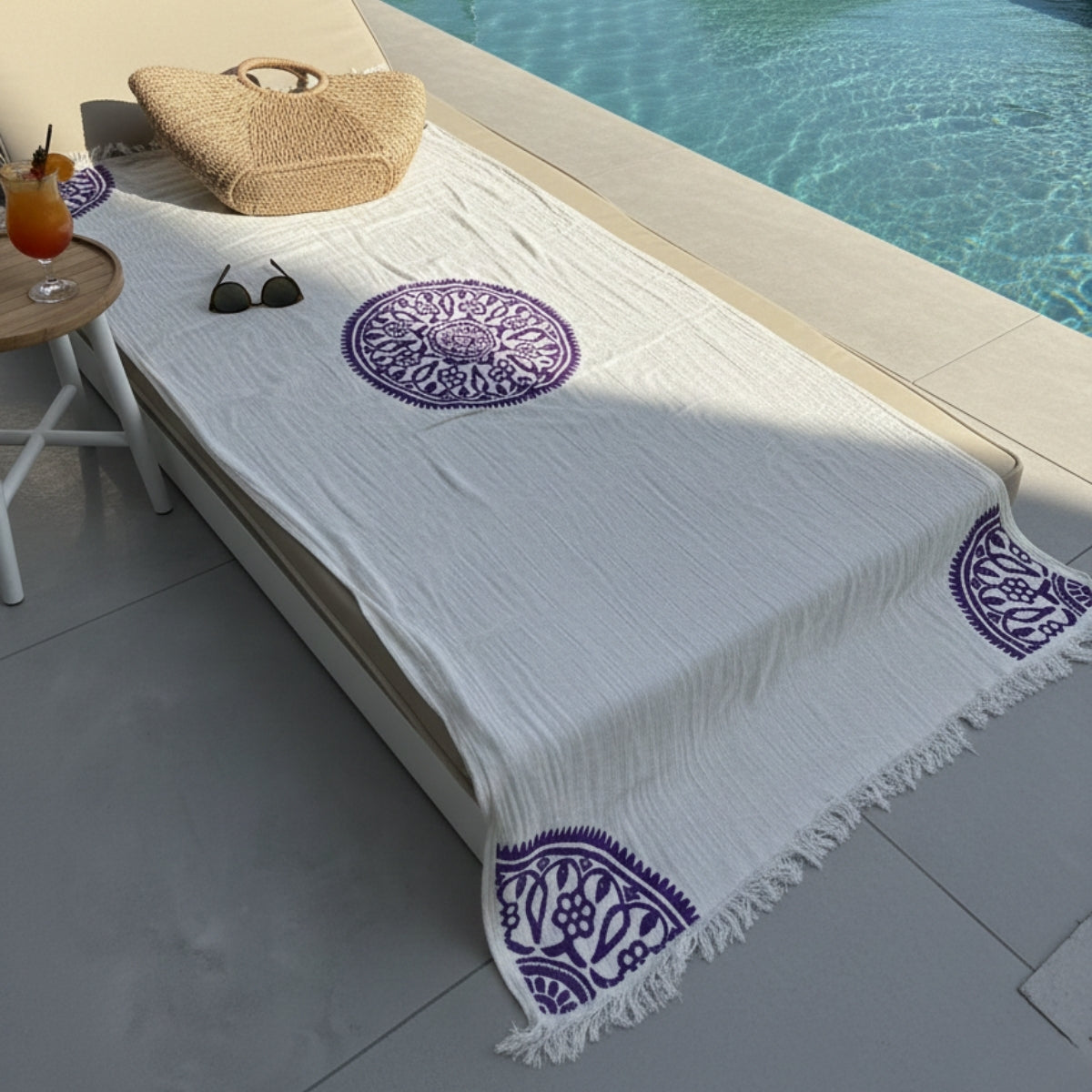 White shawl with purple patterns on a lounge chair by a poolside.