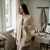 Woman wearing a cream-colored short kimono with black printed patterns in a cozy room.