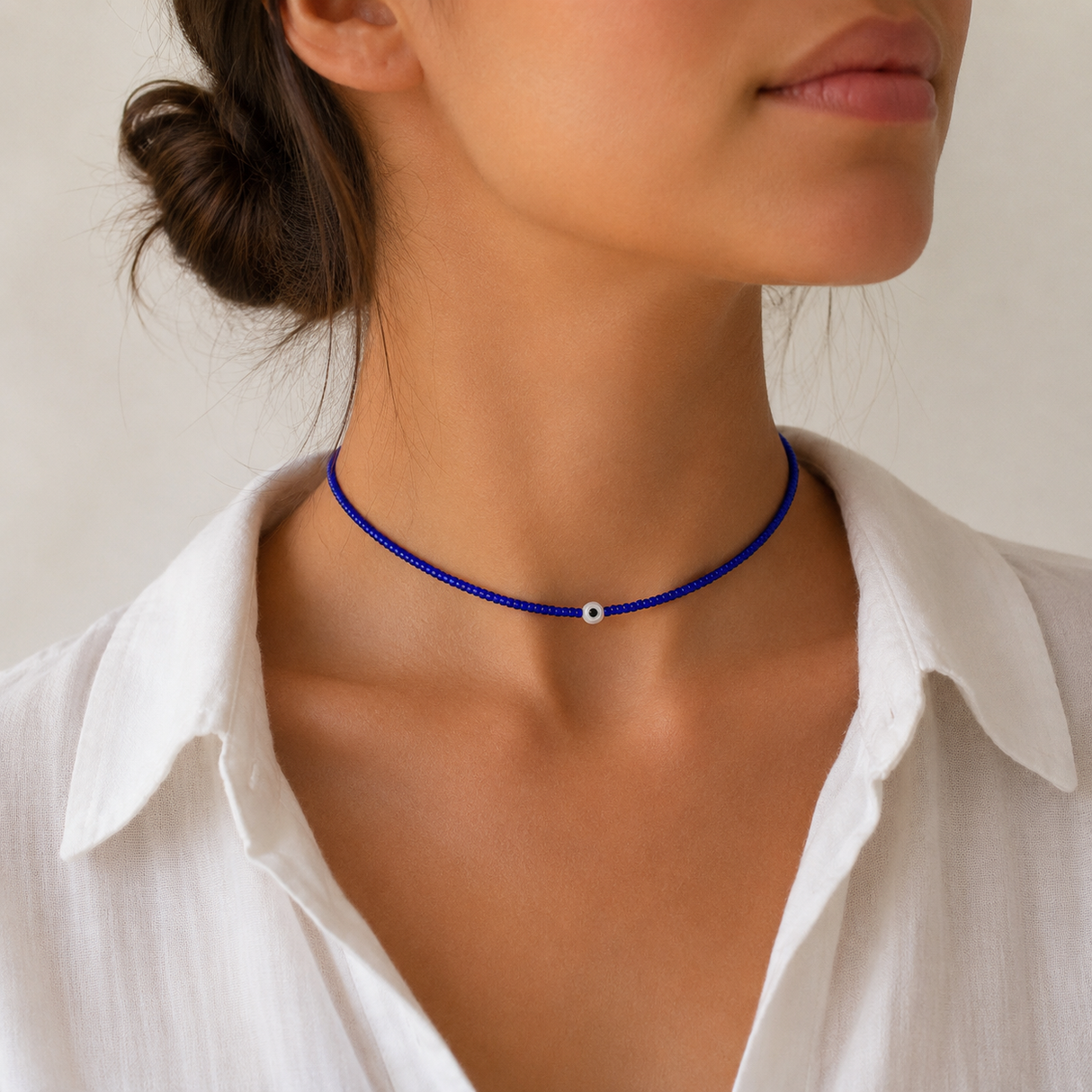 Woman wearing blue tiny beaded evil eye choker necklace with an evil eye bead, styled with a white collared shirt