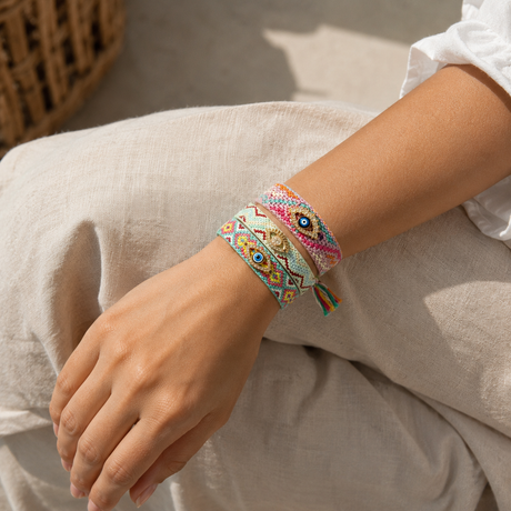 Woman wearing stacked Boho Evil Eye Friendship Bracelets in mint and pink woven patterns with gold evil eye charms, styled with tassel details on wrist for a bohemian layered look