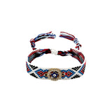 Woven friendship bracelet in white red and blue pattern with round gold evil eye pendant surrounded by pave crystals, adjustable pull cord closure