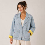 Front view of the Boutique Flo Confetti Embroidered Light Denim Jacket worn by a model with cuffed yellow sleeves, showing the relaxed boxy fit and scattered embroidery