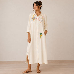 Front view of the Boutique Flo Good Vibes Embroidered White Shirt Dress worn by a model with rolled sleeves, side slit, and embroidered sun and palm tree detailing
