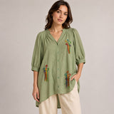 Front view of the Boutique Flo Wildflower Embroidered Green Shirt Dress worn by a model, showing multicolor hand-embroidered wildflower motifs scattered across the sage green crinkled cotton with puff sleeves and button-through front