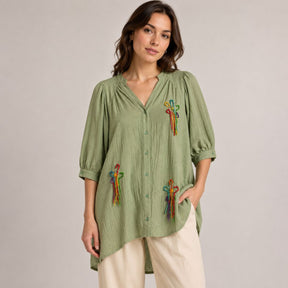 Front view of the Boutique Flo Wildflower Embroidered Green Shirt Dress worn by a model, showing multicolor hand-embroidered wildflower motifs scattered across the sage green crinkled cotton with puff sleeves and button-through front