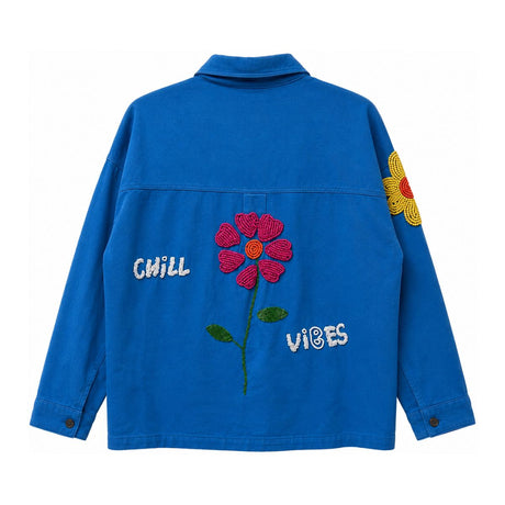 Back view of a blue cotton twill jacket with hand beaded Chill Vibes lettering and a beaded floral applique, relaxed boxy fit chore jacket with playful colorful embellishment