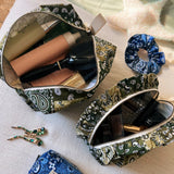 Overhead view of open Cofin Paris green bandana toiletry bags filled with beauty products, hairbrush, and accessories.