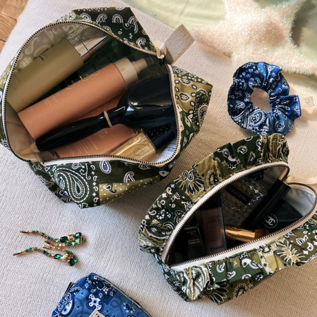 Overhead view of open Cofin Paris green bandana toiletry bags filled with beauty products, hairbrush, and accessories.