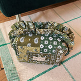 Close-up lifestyle shot of the Cofin Paris Medium Louise Green Bandana Ruffled Toiletry Bag resting on a woven rug.