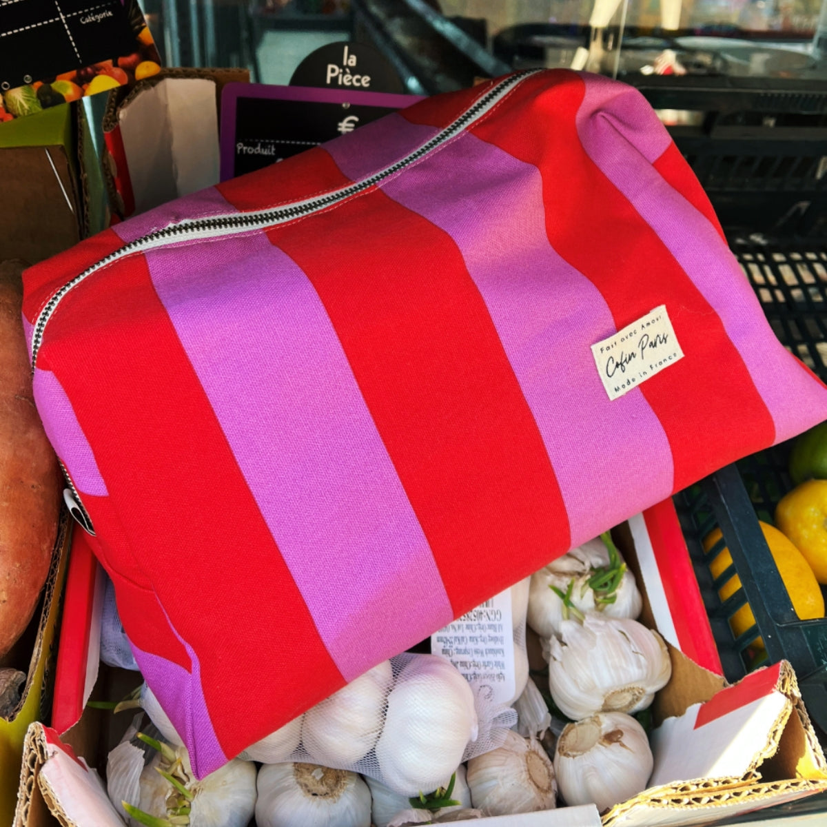 Top down view of three sizes of Cofin Paris red and pink striped toiletry bags arranged on pink cardboard boxes.