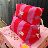 Cofin Paris extra large Paola striped toiletry pouch resting atop fresh garlic produce in a Parisian market setup.