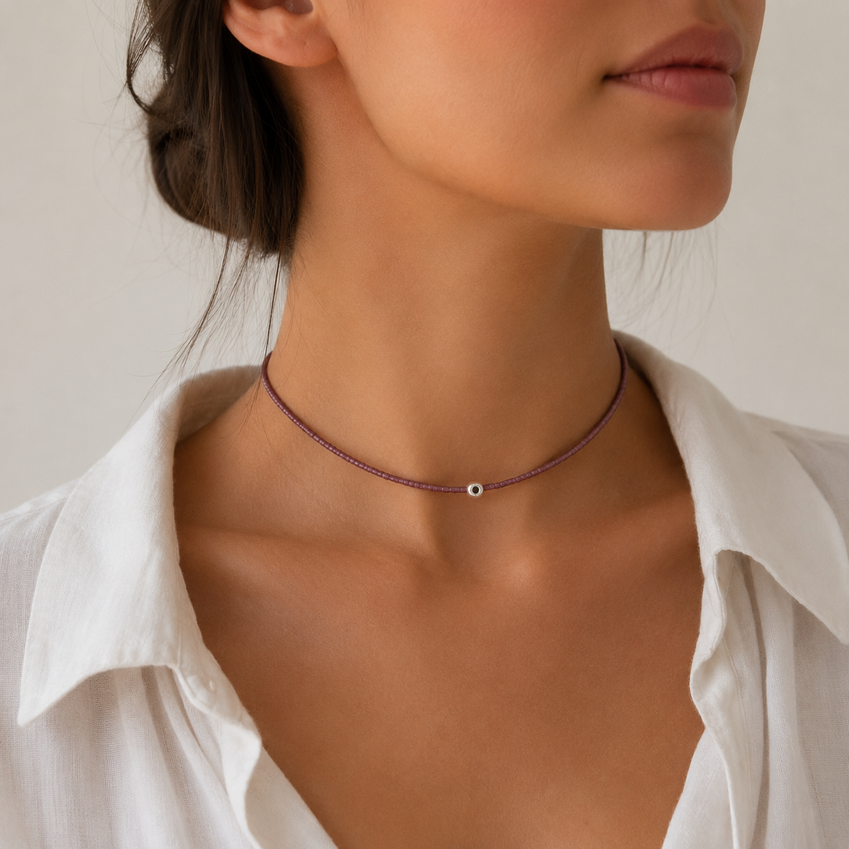 Woman wearing dark rose tiny beaded evil eye choker necklace with a silver accent bead, styled with a white collared shirt