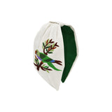 White headband hand embroidered with a green parrot perched on a branch, forest green lining visible along the inner band