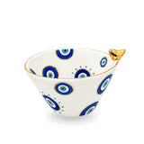 Side angle view of the white ceramic evil eye birdie bowl displaying interior and exterior painted patterns and gilded accents.