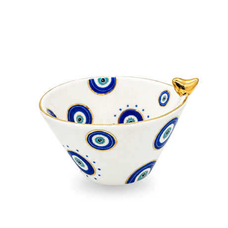 Side angle view of the white ceramic evil eye birdie bowl displaying interior and exterior painted patterns and gilded accents.