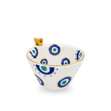 Front view of a white ceramic bowl decorated with hand-painted blue evil eye patterns, a metallic gold rim, and a small gold bird perched on the edge.