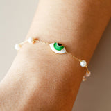 Close-up view of model wearing Orchid Jewelry 18k gold green enamel eye and pearl station bracelet on wrist