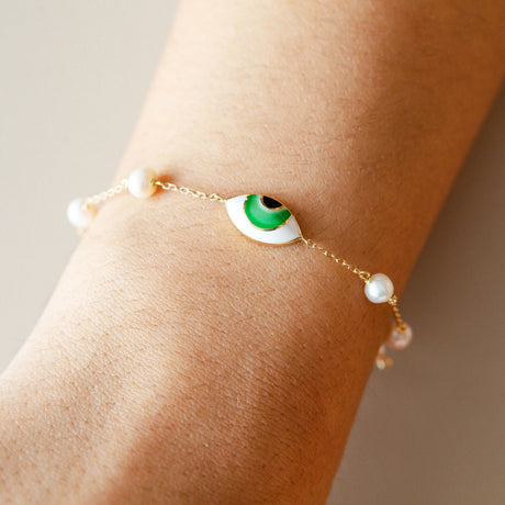 Close-up view of model wearing Orchid Jewelry 18k gold green enamel eye and pearl station bracelet on wrist