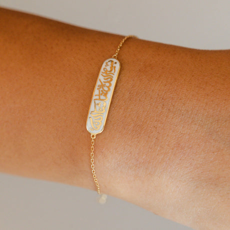 Model wearing Orchid Jewelry 18k yellow gold and white enamel Bismillah calligraphic bracelet on wrist