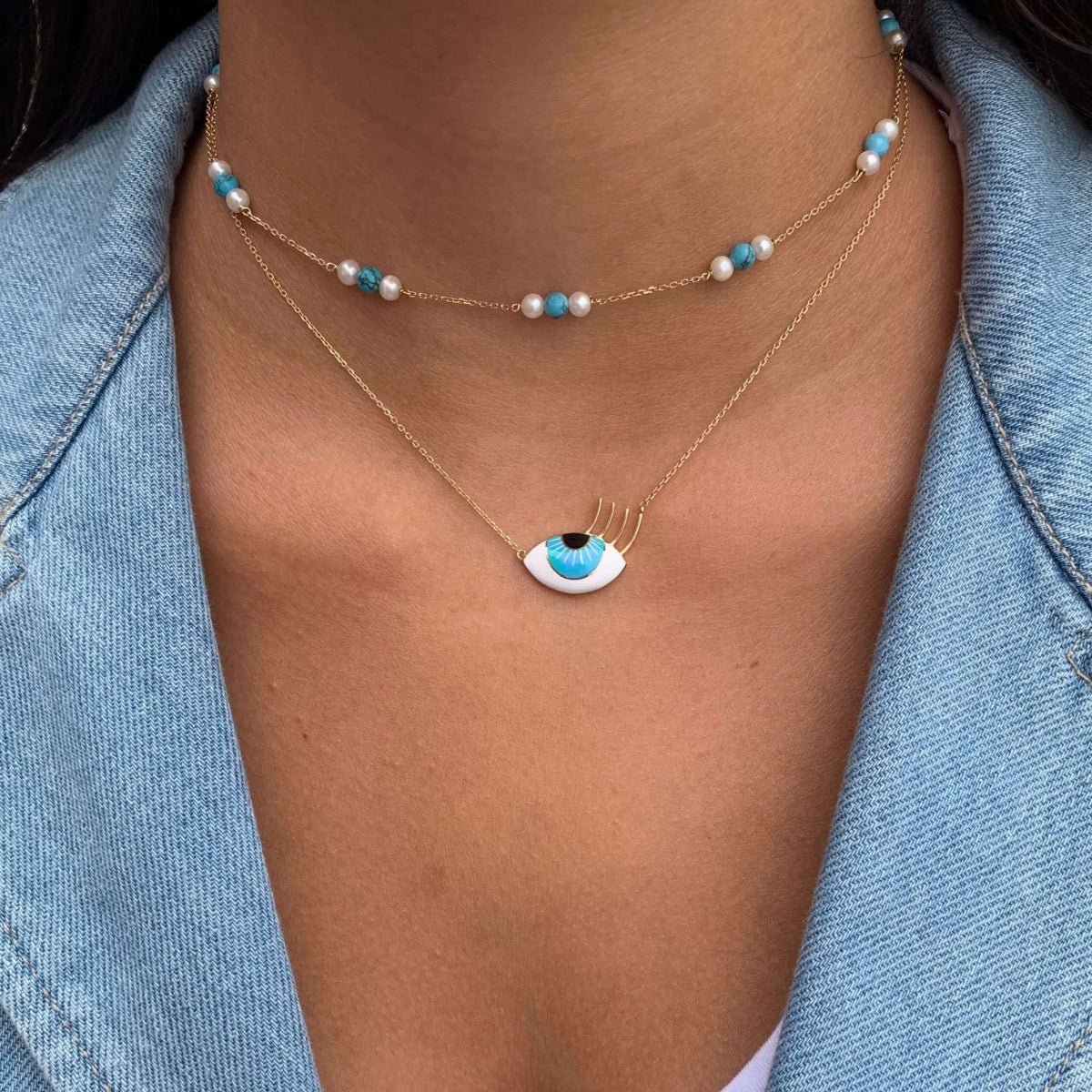 Model wearing Orchid Jewelry 18k gold flirty aqua eye necklace layered below a turquoise and pearl station choker