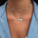 Model wearing Orchid Jewelry 18k gold flirty aqua eye necklace layered below a turquoise and pearl station choker