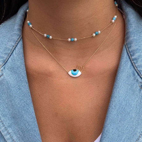 Model wearing Orchid Jewelry 18k gold flirty aqua eye necklace layered below a turquoise and pearl station choker