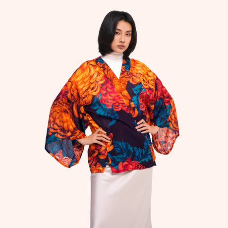 Model wearing an orange and teal chrysanthemum print kimono jacket over a white turtleneck, wide draped sleeves shown from the front