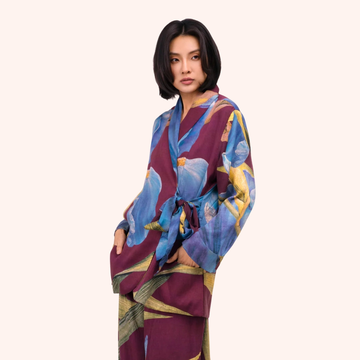 Model wearing a plum wrap jacket with periwinkle blue and gold iris print, side tie closure at the waist