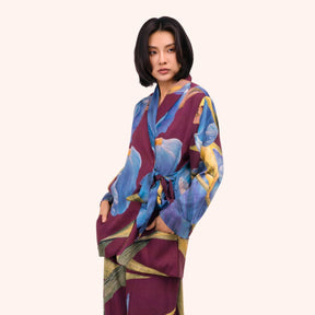 Model wearing a plum wrap jacket with periwinkle blue and gold iris print, side tie closure at the waist