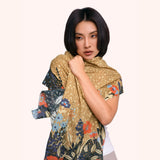 Model wearing the moss gold floral hedgerow scarf draped around the shoulders, showing the coral and blue floral print against the navy border