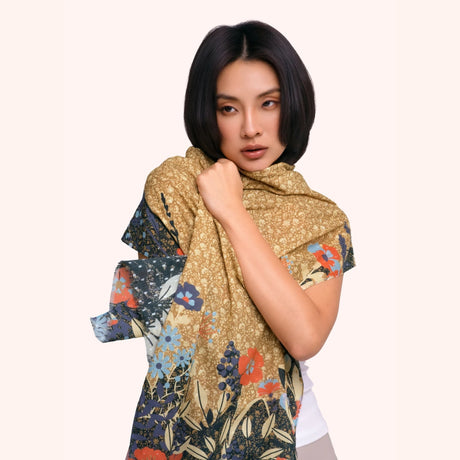 Model wearing the moss gold floral hedgerow scarf draped around the shoulders, showing the coral and blue floral print against the navy border