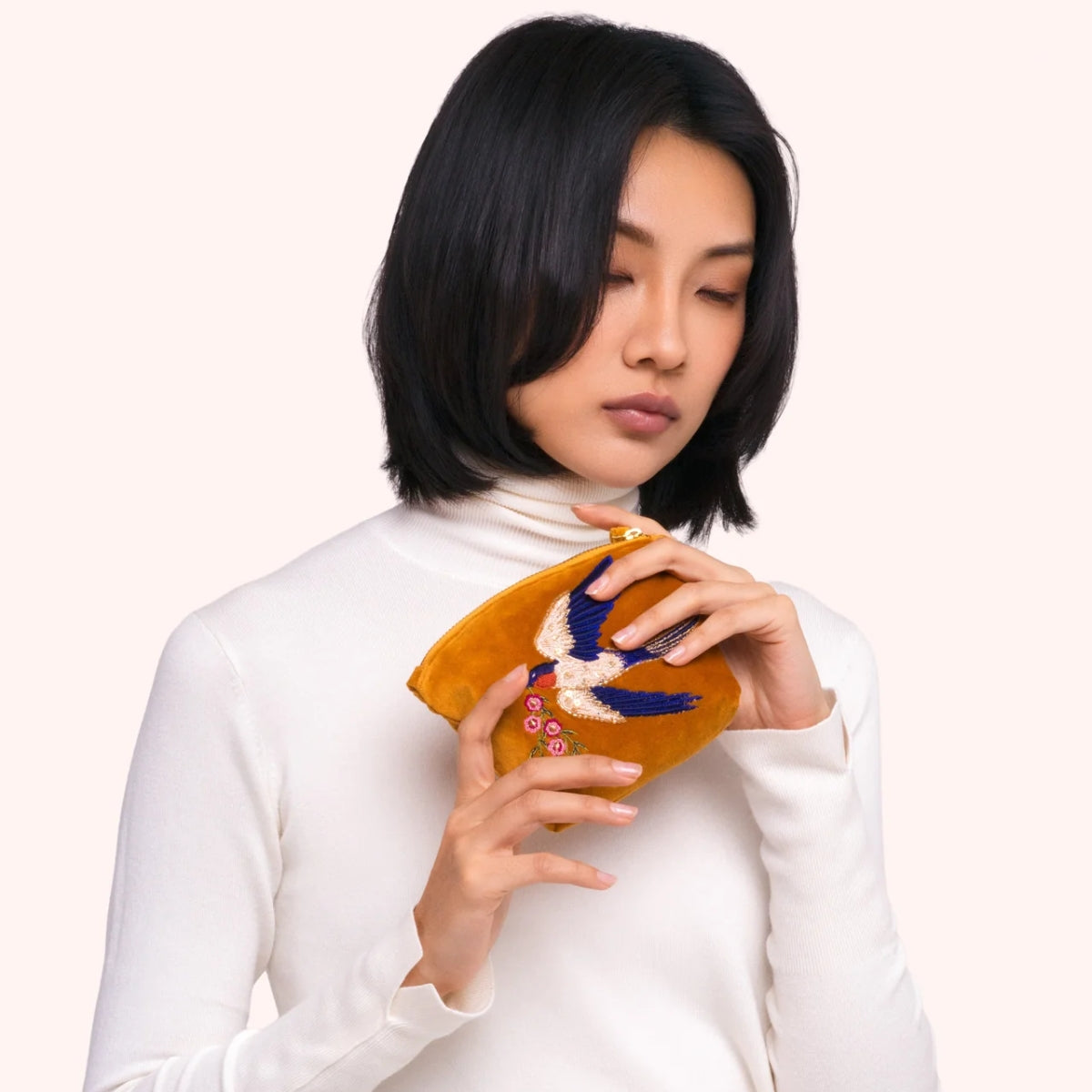 Model holding the mustard velvet swallow mini pouch, showing the beaded bird and floral embroidery up close