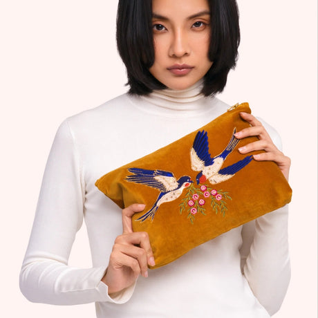 Model holding the mustard velvet swallow zip pouch, showing the beaded bird and floral embroidery up close