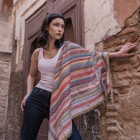 Model posing against an old brick doorway with SEP beige multicolor keffiyeh scarf draped open across her shoulder