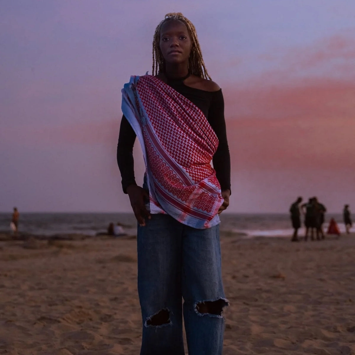 Model at the beach during sunset wearing SEP blue and red keffiyeh scarf styled draped across her torso