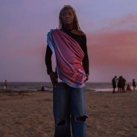 Model at the beach during sunset wearing SEP blue and red keffiyeh scarf styled draped across her torso